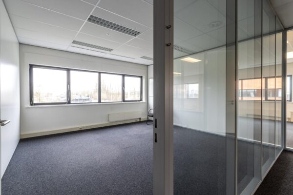 Leeg kantoorpand aan de Lage Biezenweg met glazen scheidingswanden en grote ramen.